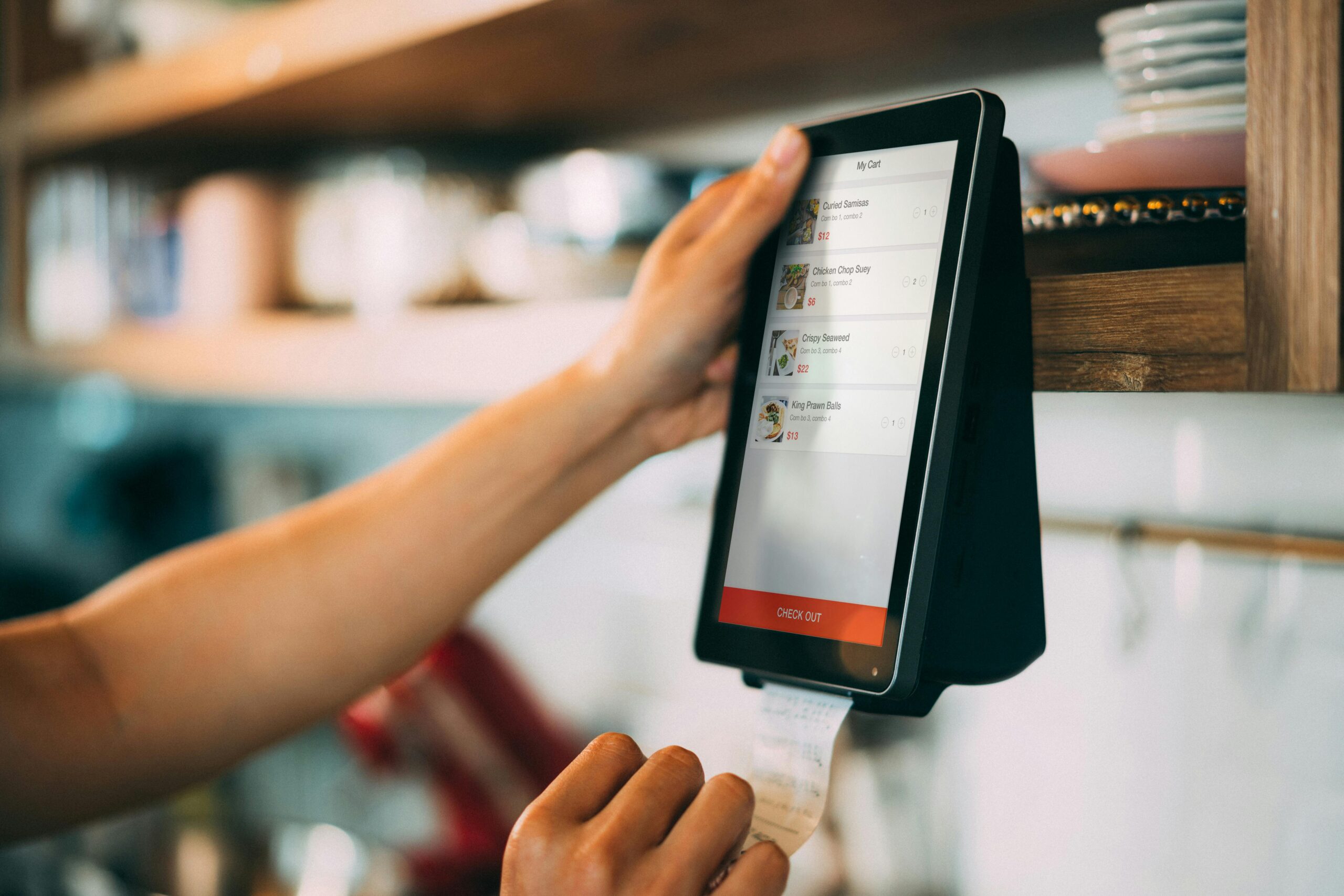 A hand uses a touchscreen digital payment system to process a receipt at a cafe.