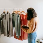 A woman selects garments from a rack in a cozy boutique, holding a notepad.