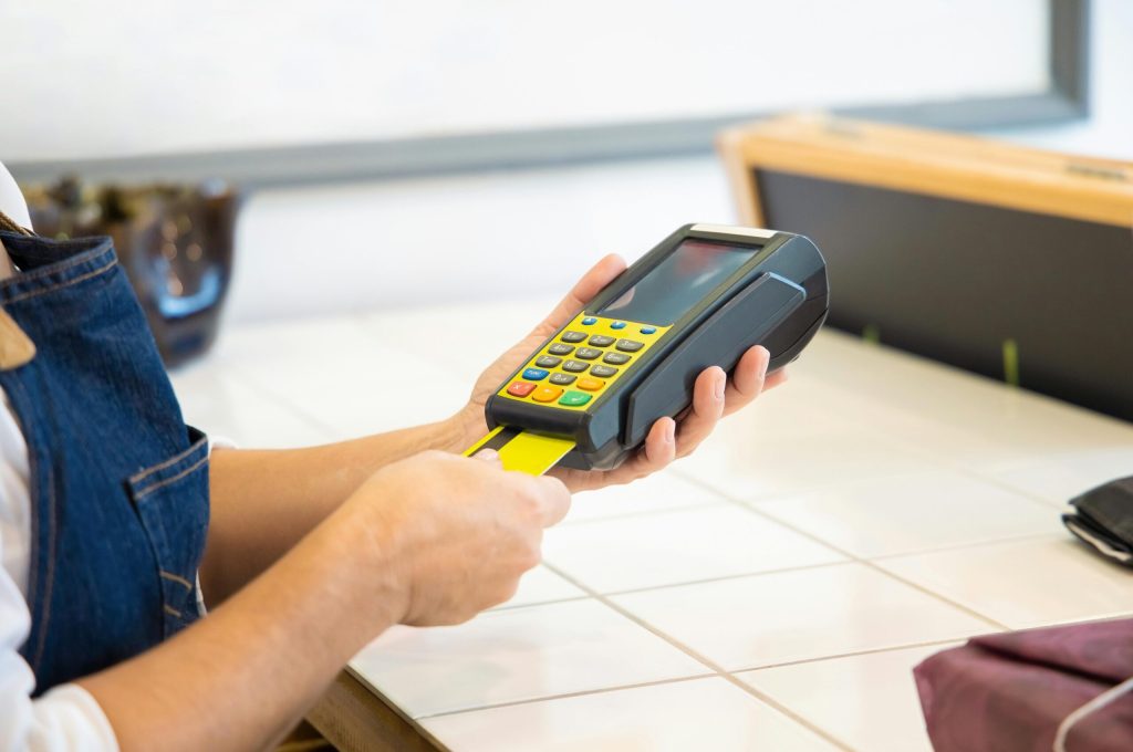 pexels-photo-6023605-6023605 Close-up of hands operating a credit card POS machine in a commercial setting.