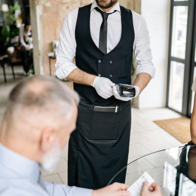 A waiter processes payment using a terminal while a customer reviews the bill, showcasing excellent service.