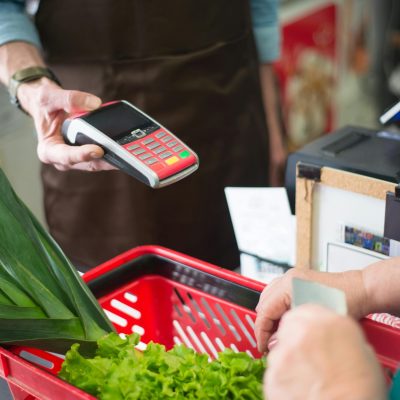 A customer using a contactless payment method at a grocery store checkout with fresh produce.